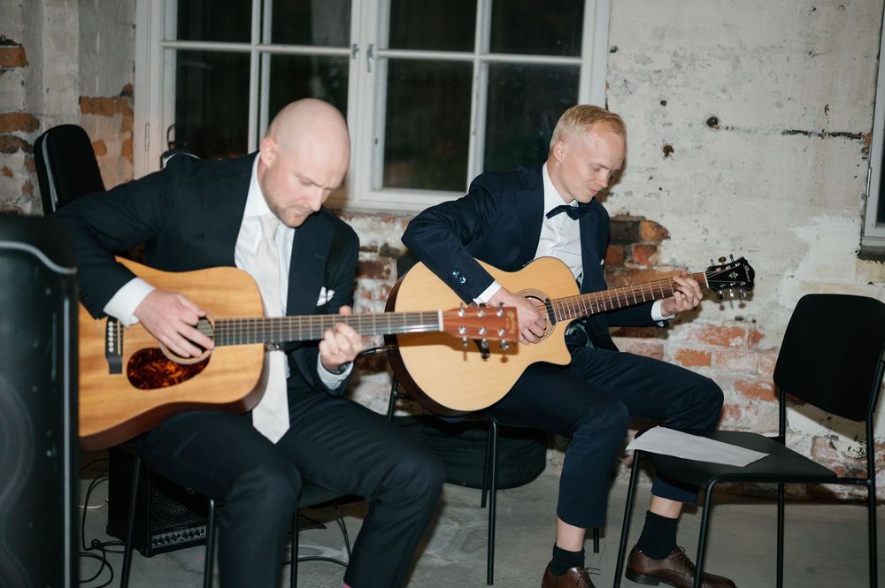 Acoustic guitar performers entertain guests at a wedding reception in an industrial venue.