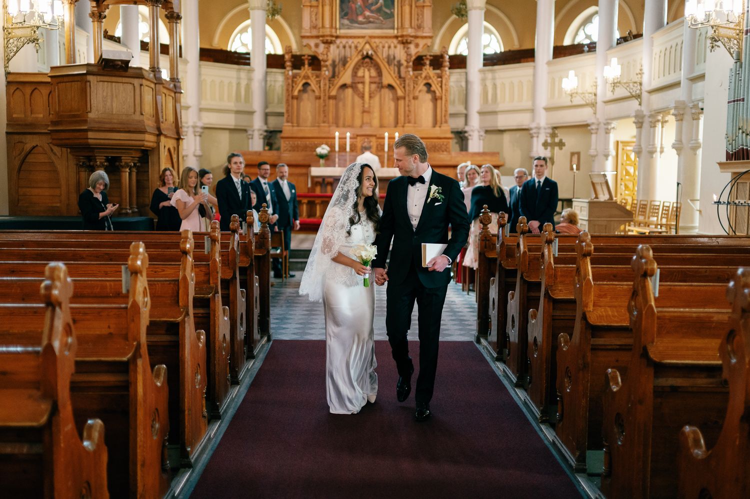 Bride and groom walking down the aisle of an ornate church after their wedding ceremony.