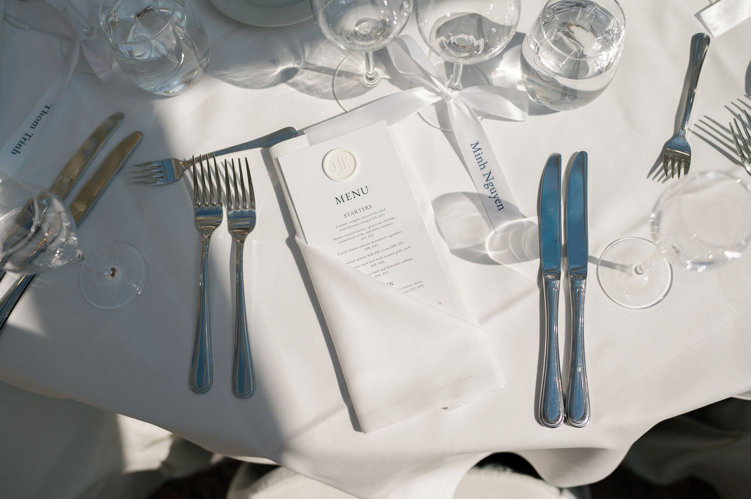 Elegant table setting with blue cutlery, crystal glasses, and a menu card on a white linen tablecloth.