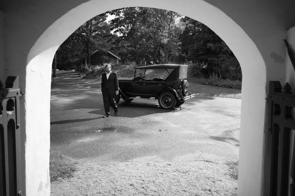 Vintage car seen through white archways at a wedding venue.