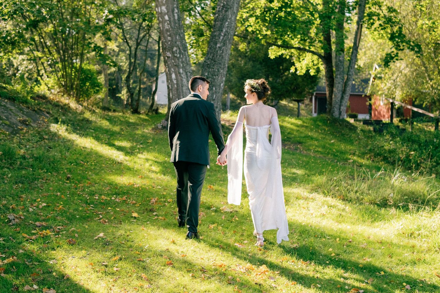 Wedding couple walks through a sunlit garden path surrounded by lush greenery.