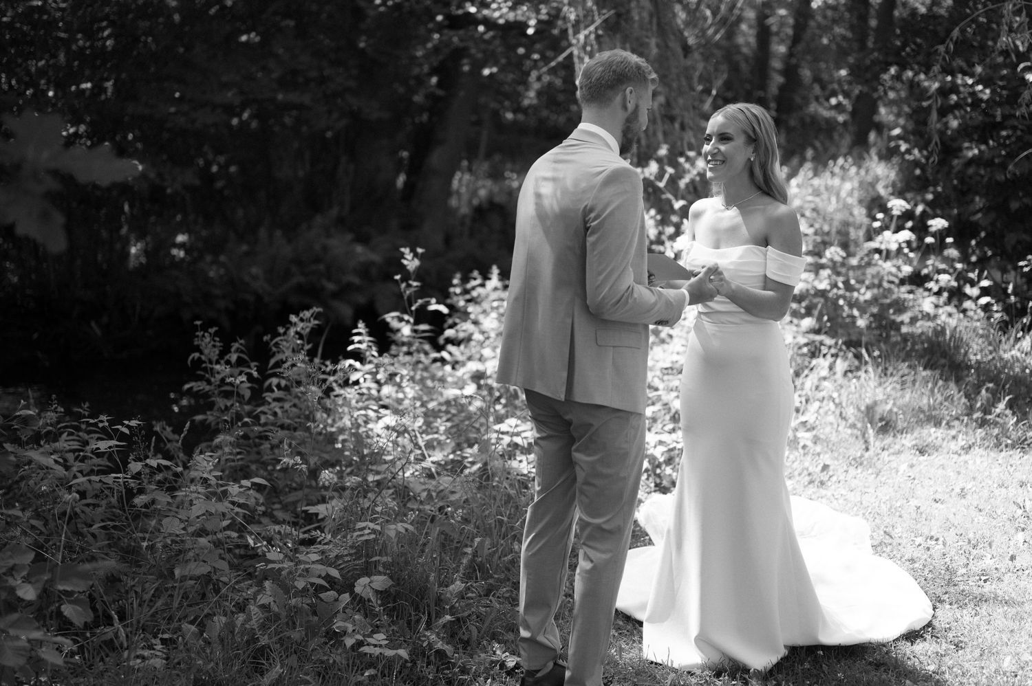 A couple stands together reading personal letters in a sun-dappled forest setting.