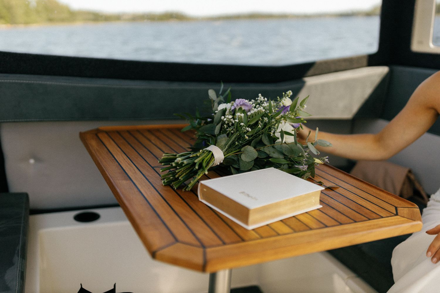 Wooden table on a boat deck with a floral arrangement and book.