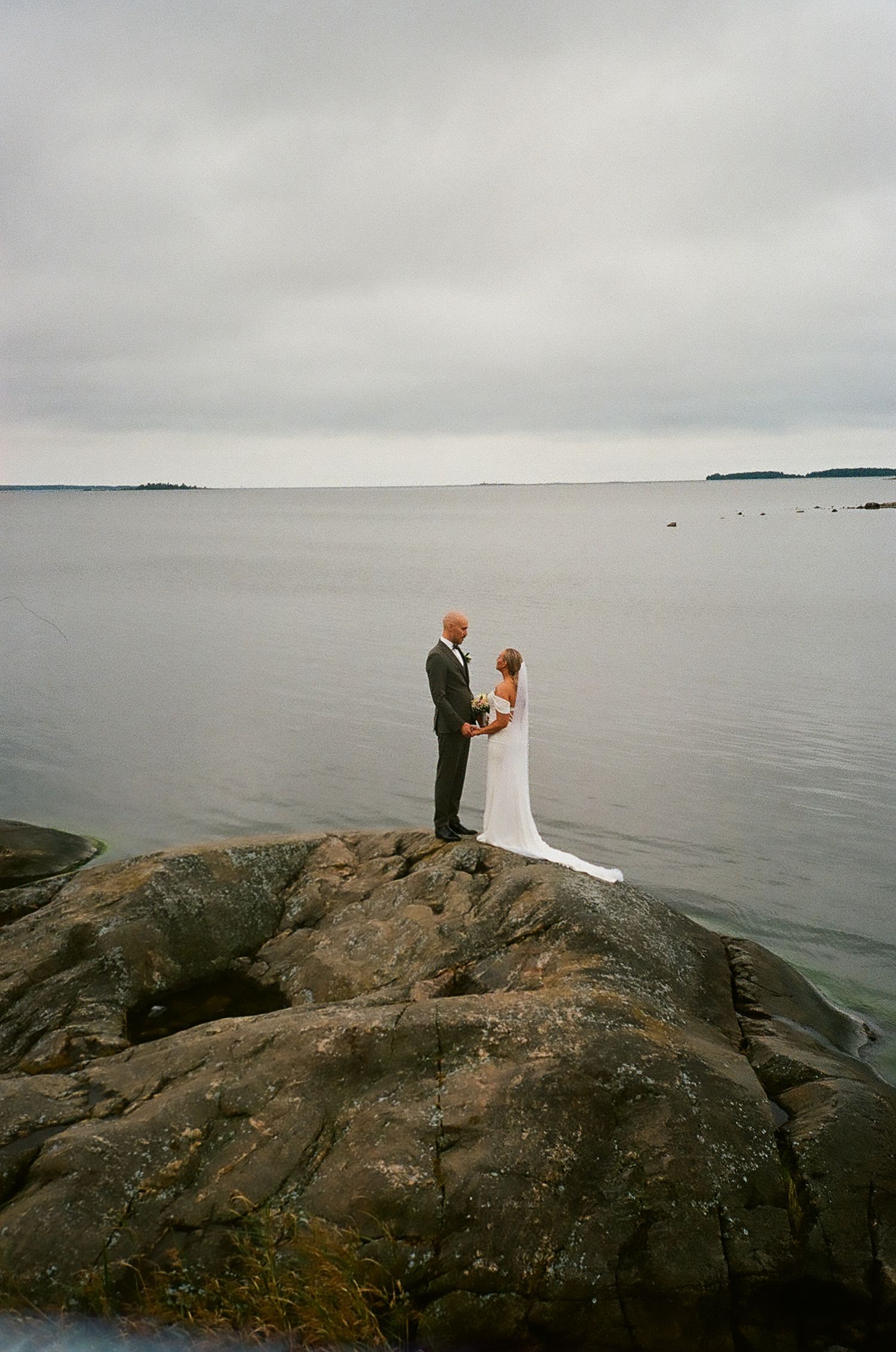 Couple standing on rocky shore overlooking misty ocean horizon.