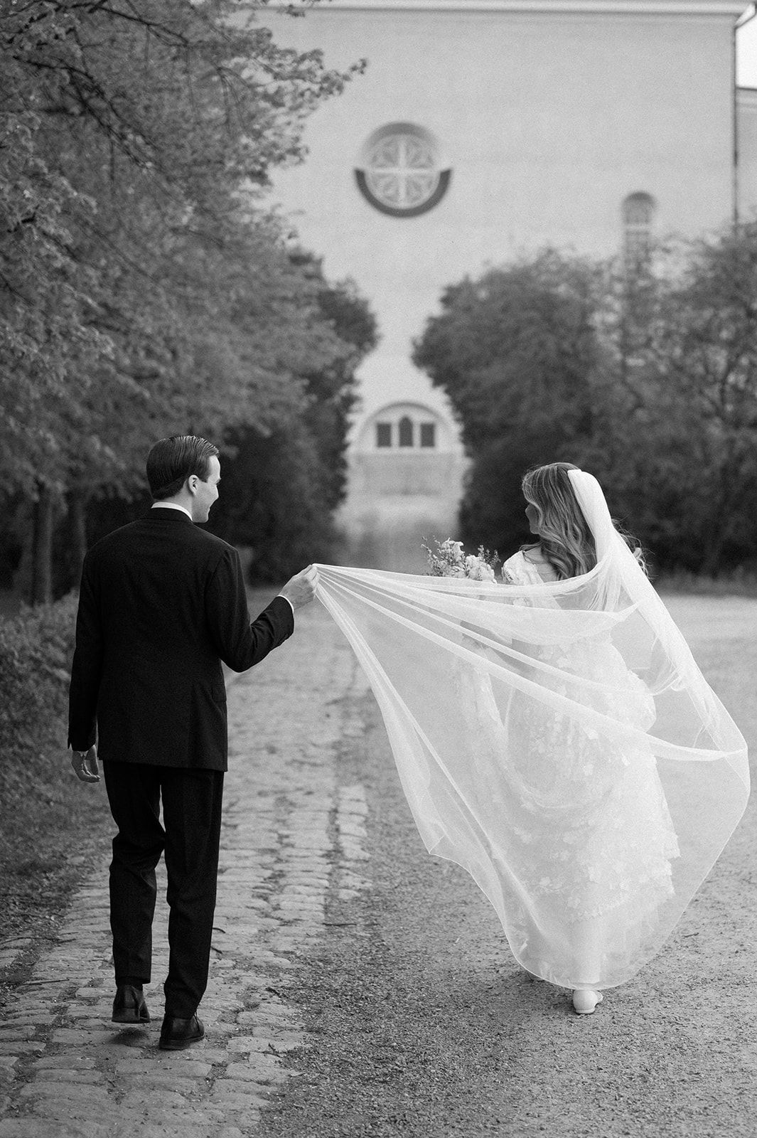 Dramatic wedding photos showing couple walking along tree-lined path with flowing veil.