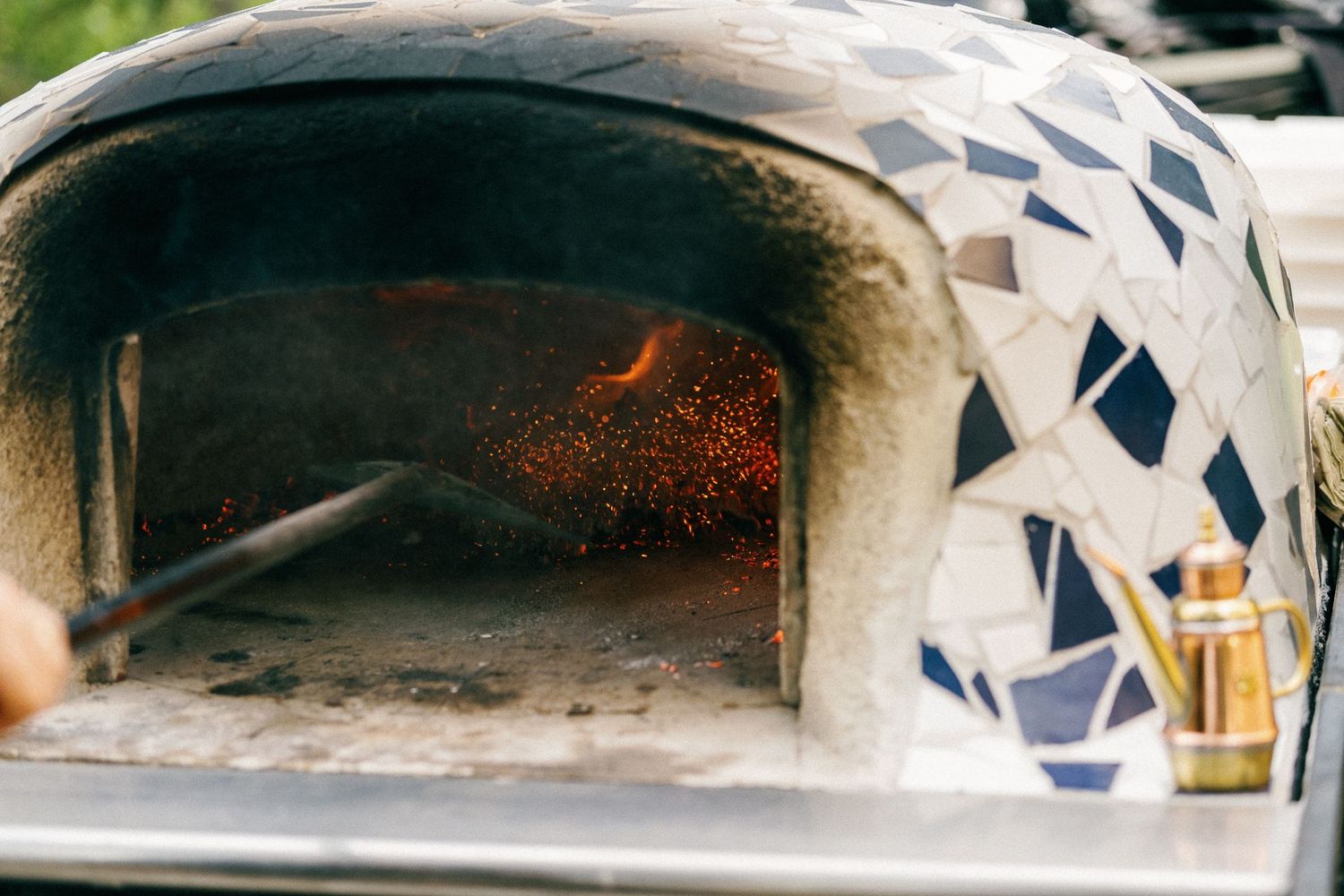 Close-up view of a mosaic-decorated pizza oven with flames visible inside.