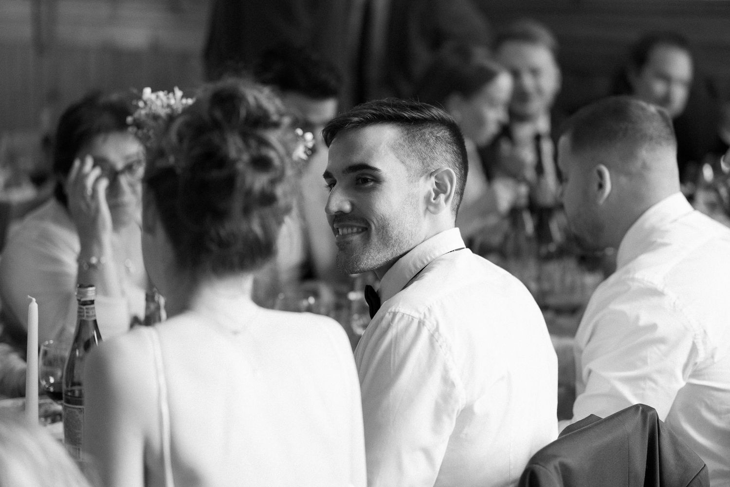 Black and white photo of wedding guests mingling and dining at an indoor reception.