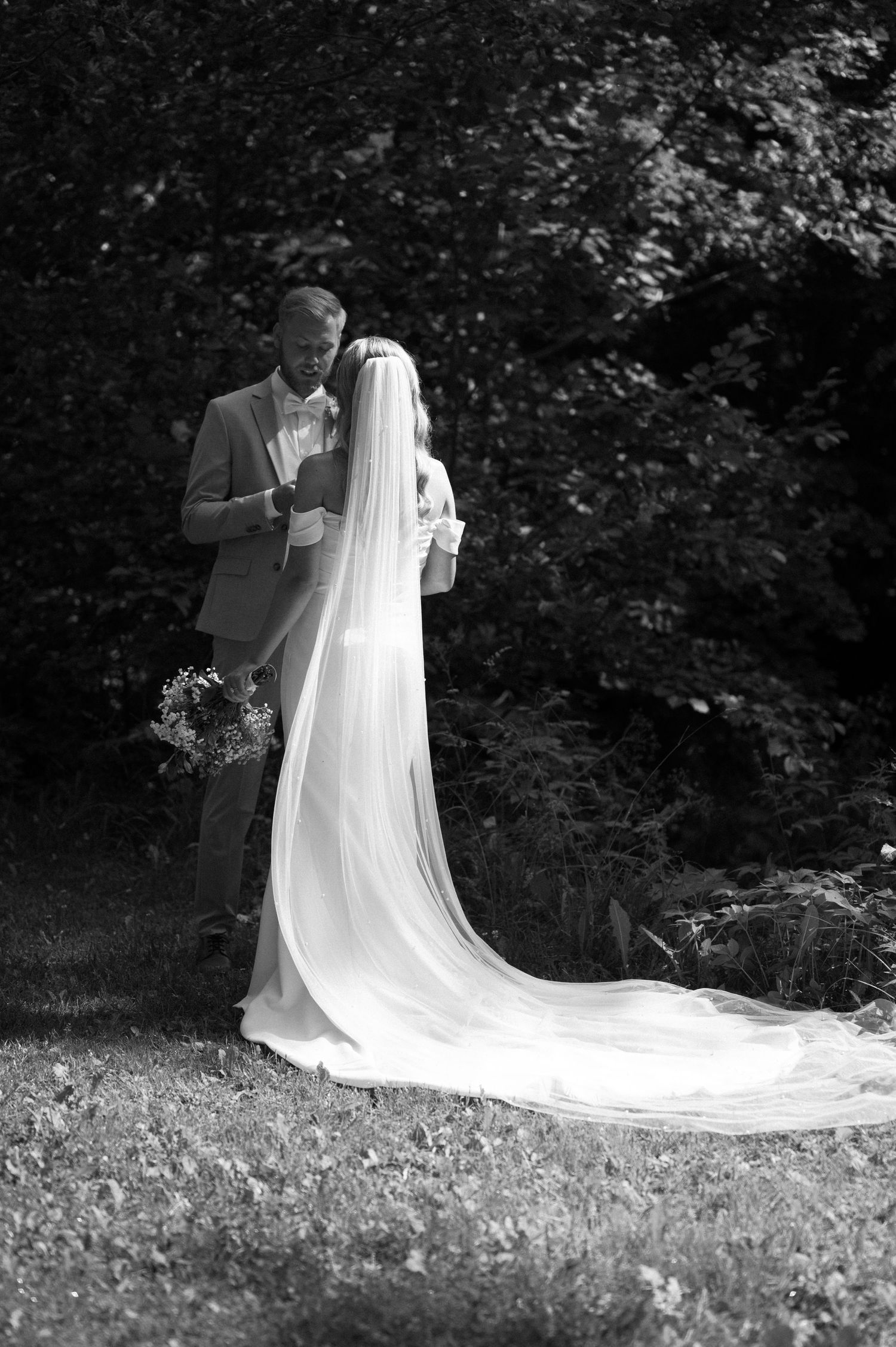 A flowing white wedding dress train trails beautifully across a grassy outdoor setting in black and white.