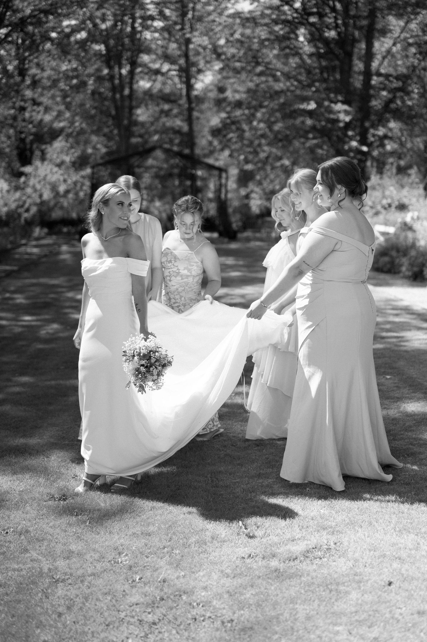 Black and white photo of wedding party sitting together on grass during outdoor celebration.