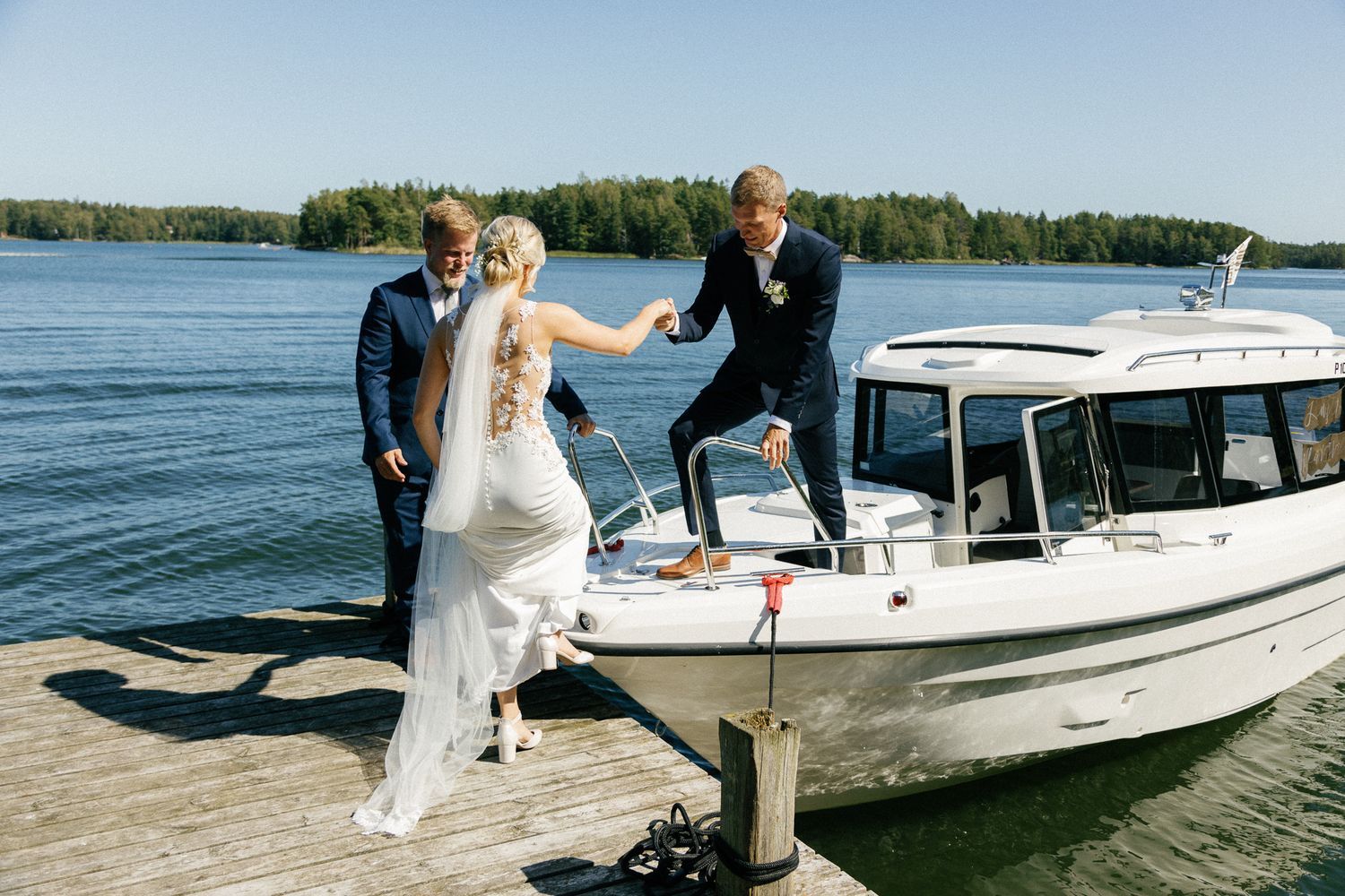 People board a white boat at a wooden dock on a sunny lake day.