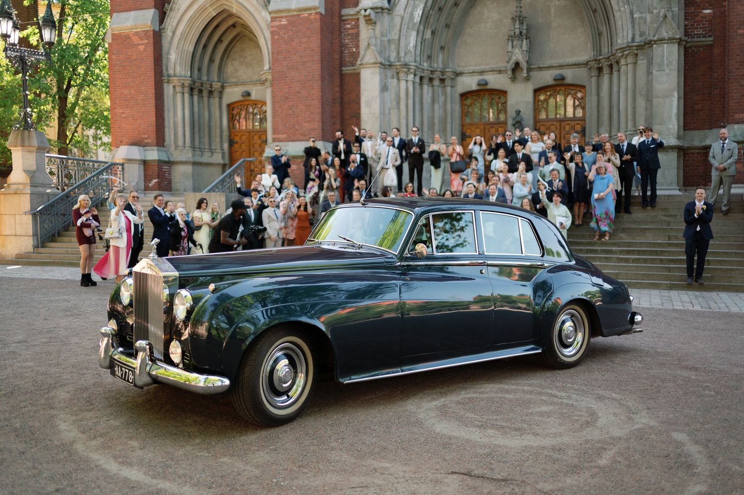 Vintage dark green Rolls-Royce wedding car parked outside a grand church with wedding guests gathered on the steps.