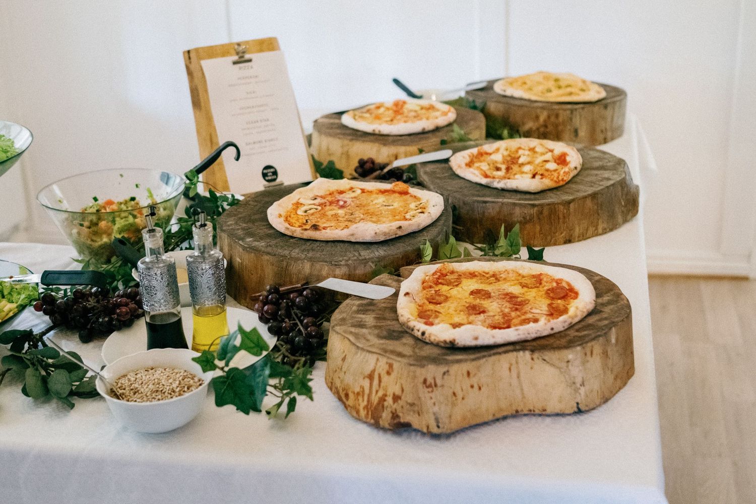 Rustic display of pizzas served on wooden log slices with greenery decorations.