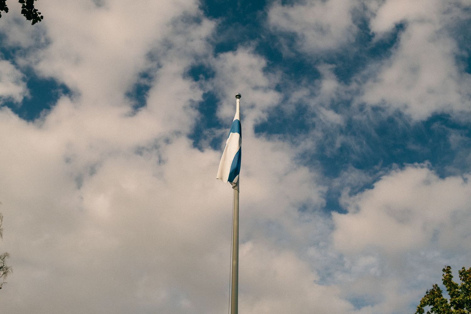 Blue sky with white puffy clouds and a tall flagpole on a sunny day.