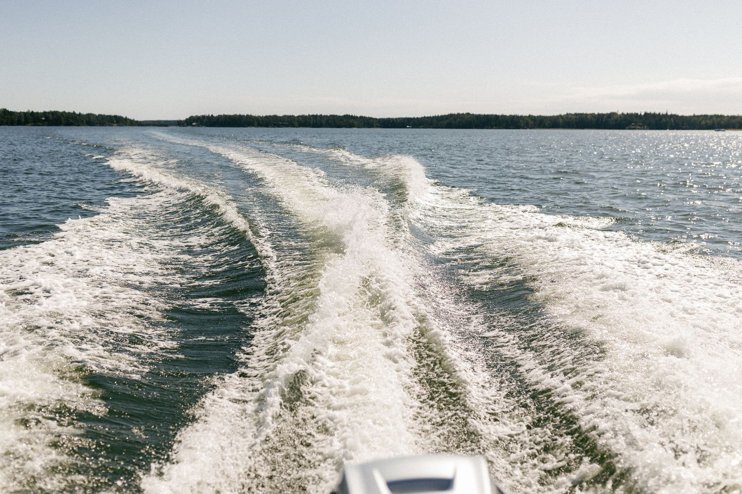 Wake patterns from boats create white trails across a blue lake on a sunny summer day.