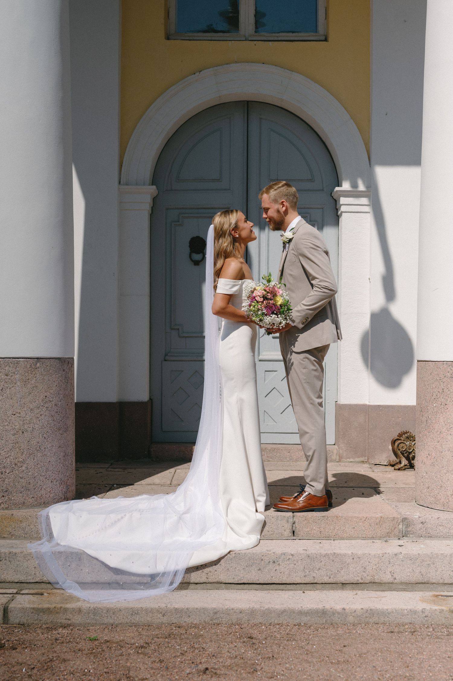 Elegant wedding portraits against a yellow building with white columns and blue doors.