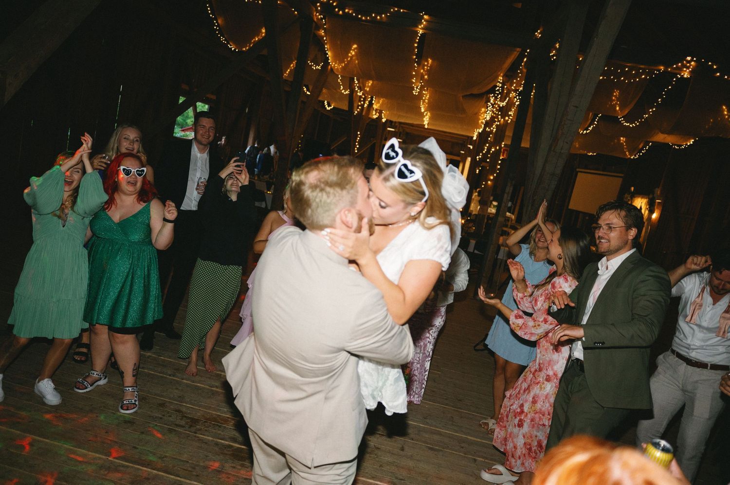 Guests dancing and celebrating at a dimly lit wedding reception with twinkle lights overhead.