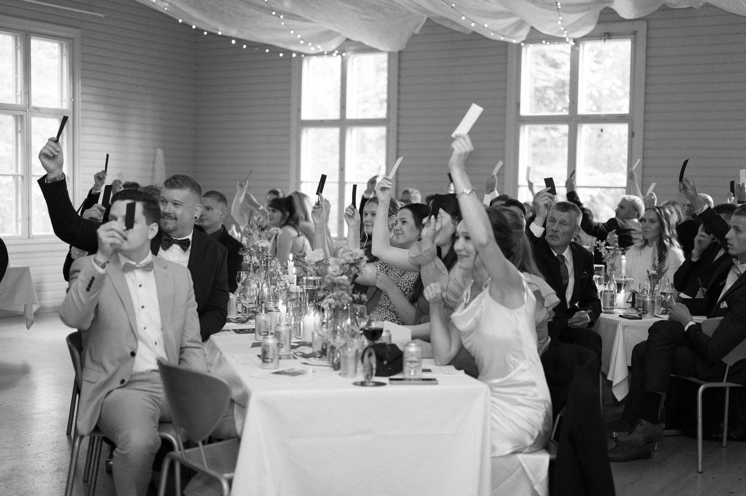 Wedding reception hall with white draped ceiling and guests celebrating with raised arms.