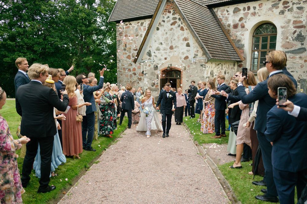 Wedding guests throw confetti along a stone church path during a joyous celebration.