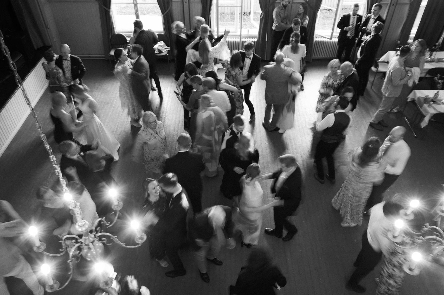 Black and white aerial view of people dancing at a wedding reception with string lights illuminating the dance floor.