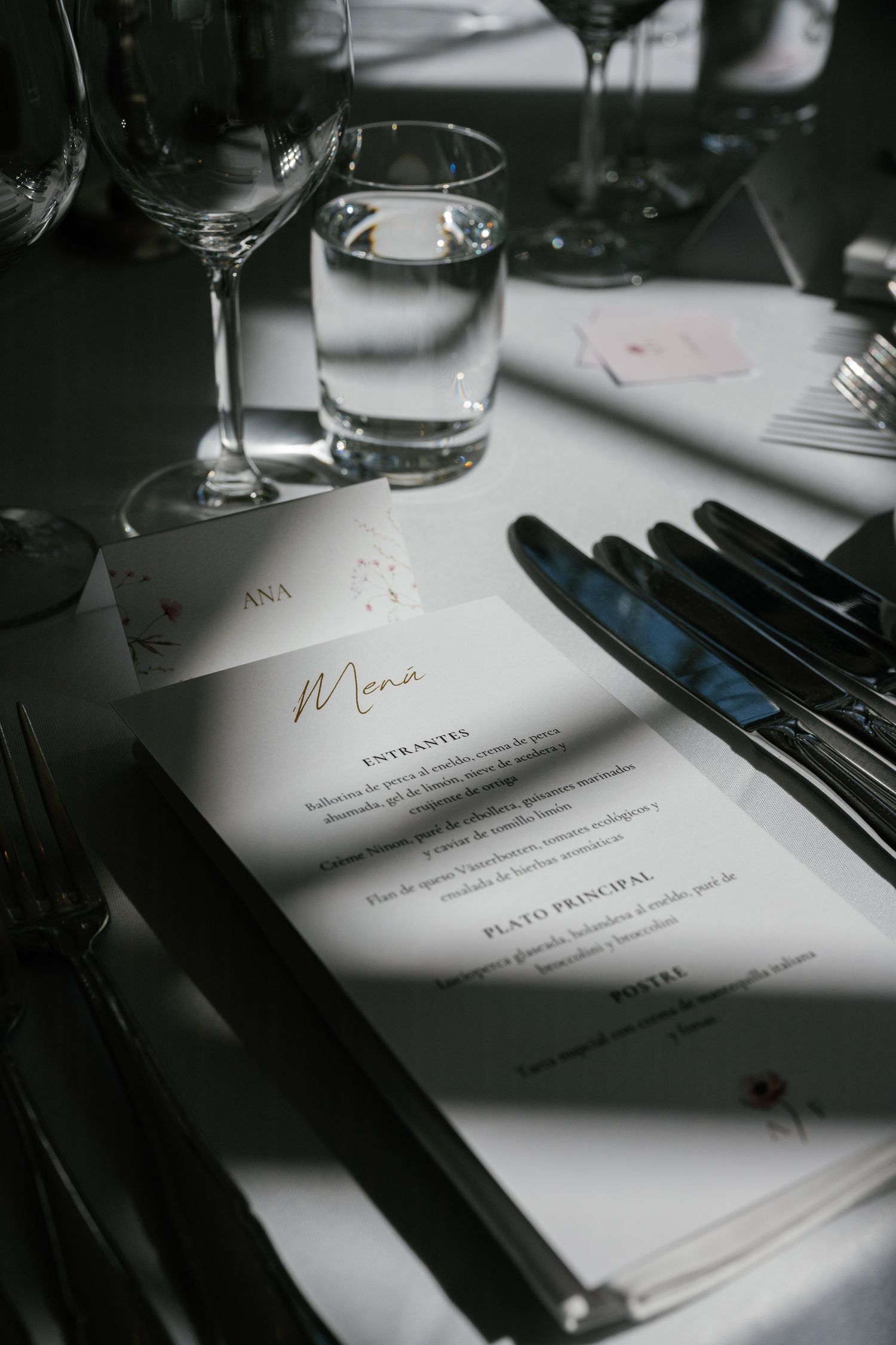 Elegant wedding table setting with menu card, crystal glasses, and silverware on white linen tablecloth.