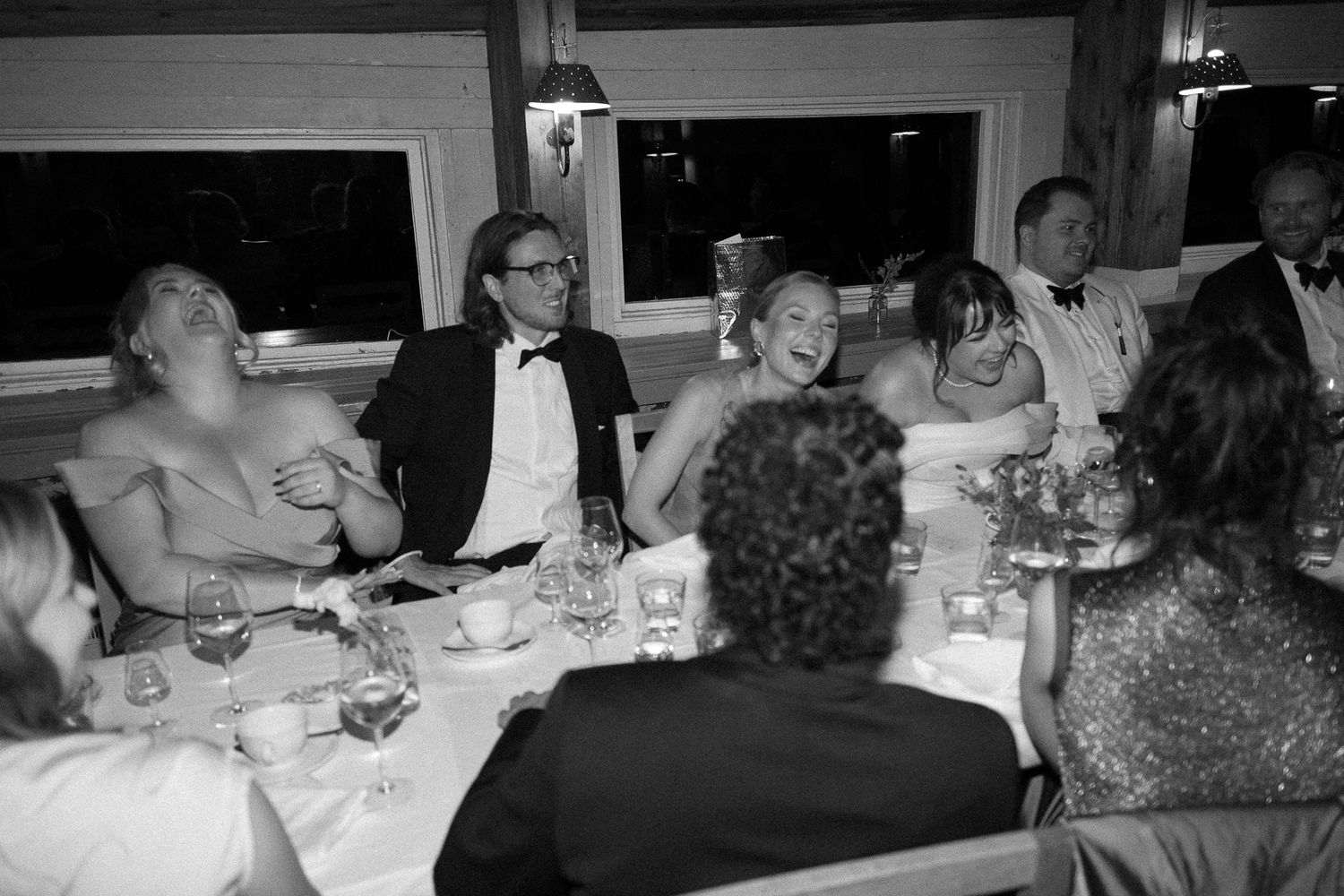 Black and white photo of elegantly dressed guests laughing at a formal dinner party event.