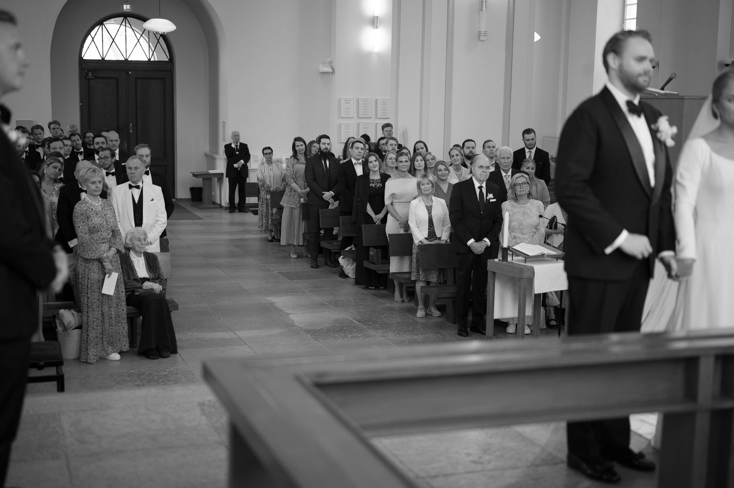 Wedding guests seated in rows at a church ceremony watching the proceedings in black and white.