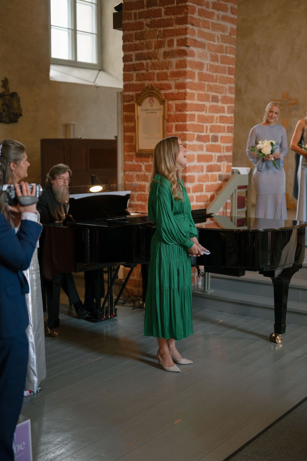 Musicians gather around a grand piano in a historic brick church setting.