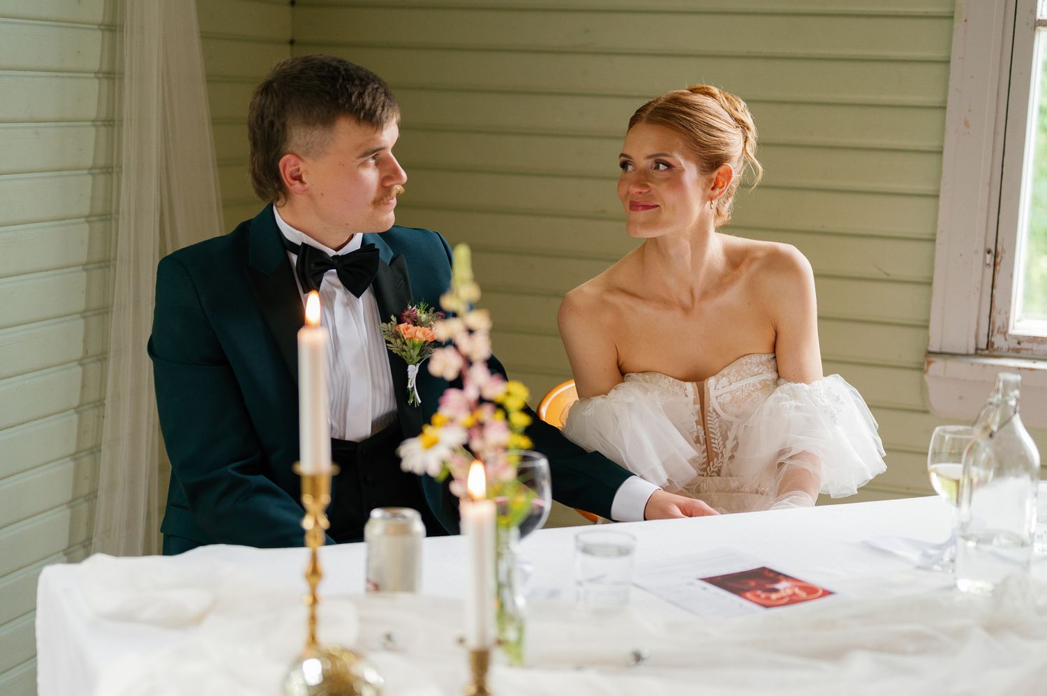 Elegant wedding reception table setting with white linens, floral centerpieces and candlelight in a bright room.