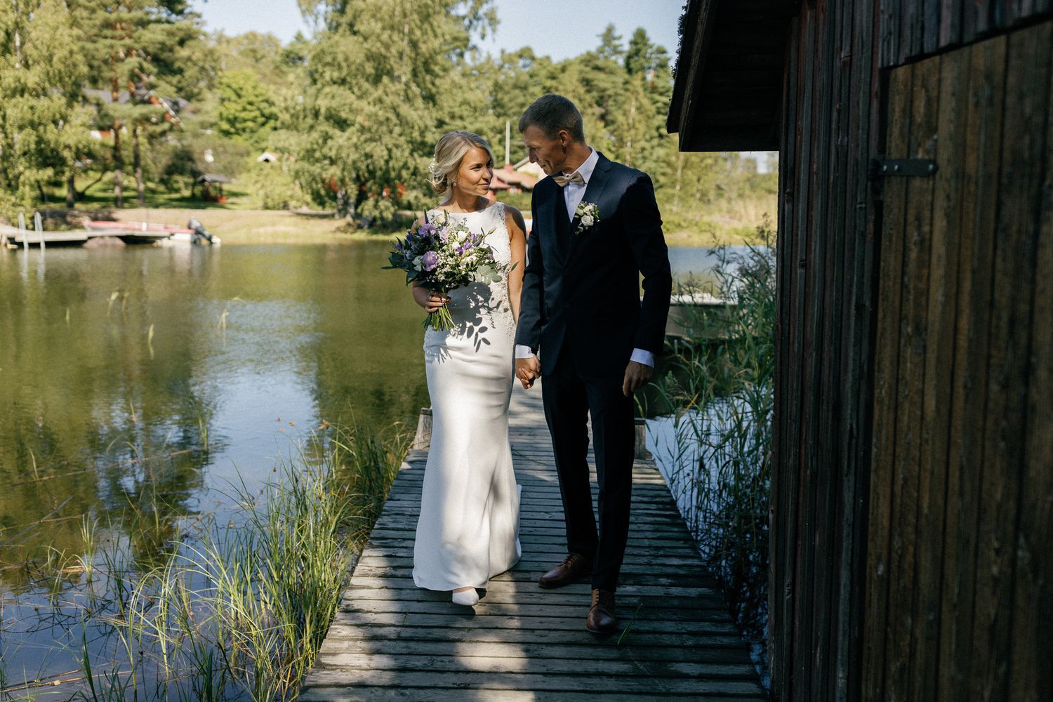 Wedding photography session on wooden dock by serene lake with pine trees in background.