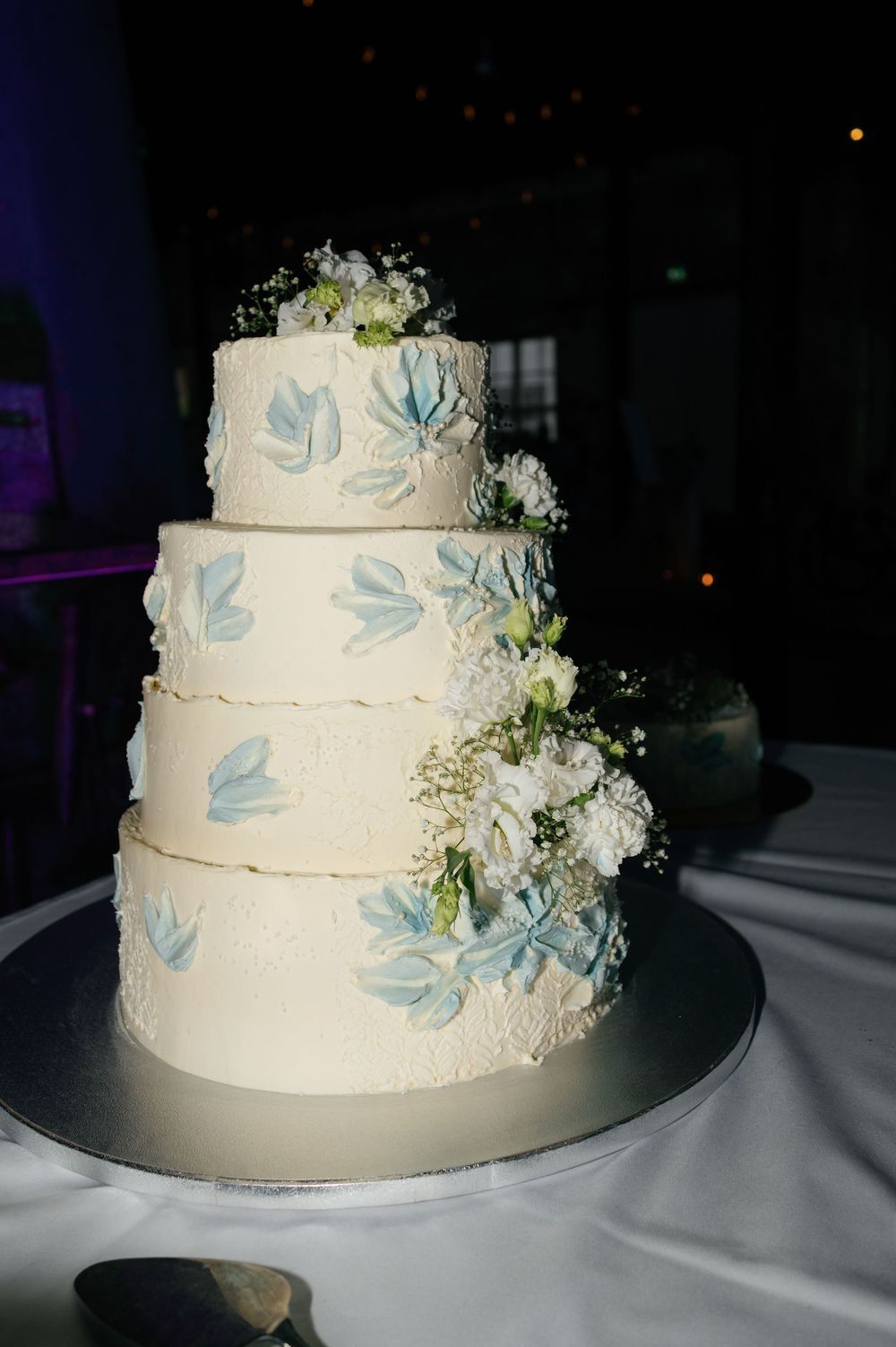 Three-tiered white wedding cake decorated with light blue accents and fresh flowers.
