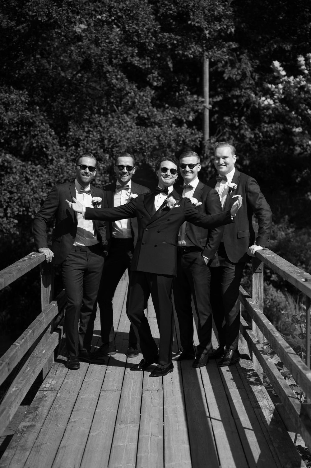 Group wearing sunglasses and formal attire posing on wooden deck.