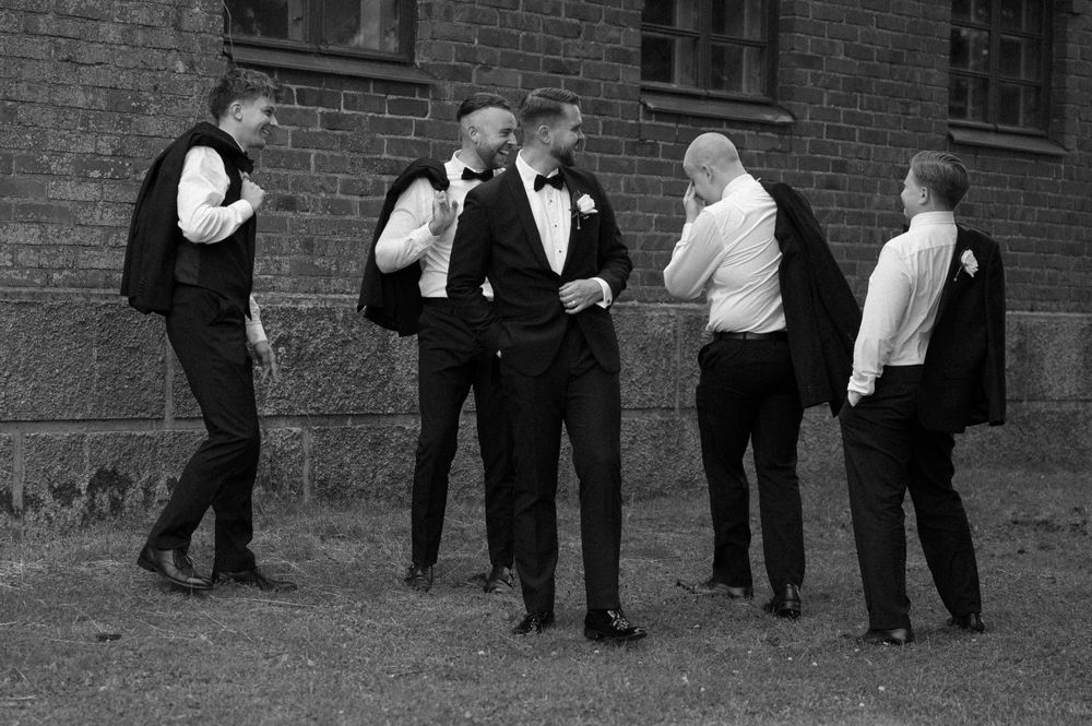 Wedding party members in formal attire walking along brick building exterior.