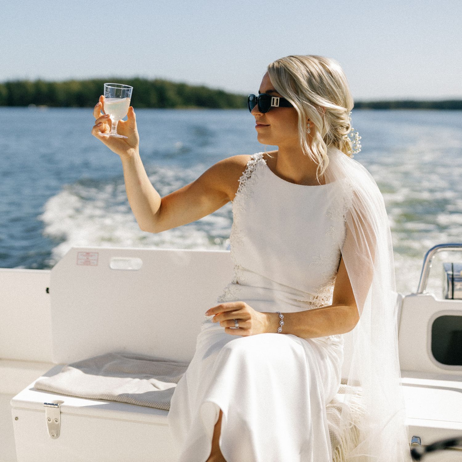 Elegant woman in white dress enjoying a drink on a boat deck during a sunny afternoon.