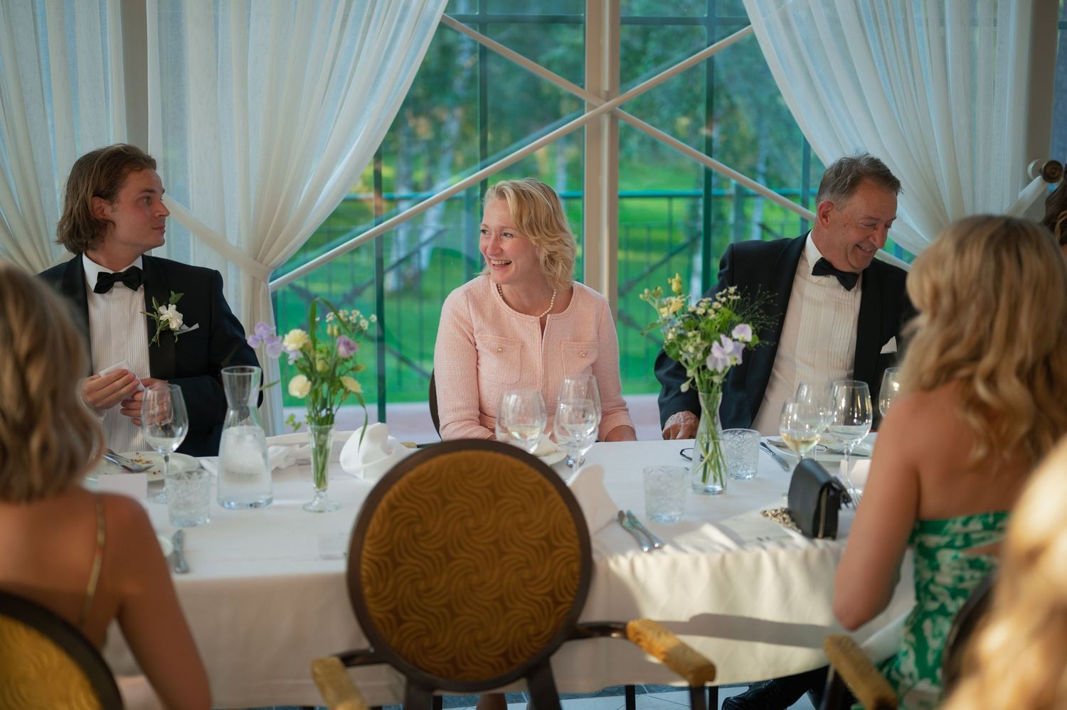 Wedding reception guests enjoying dinner at elegantly decorated tables with floral centerpieces.