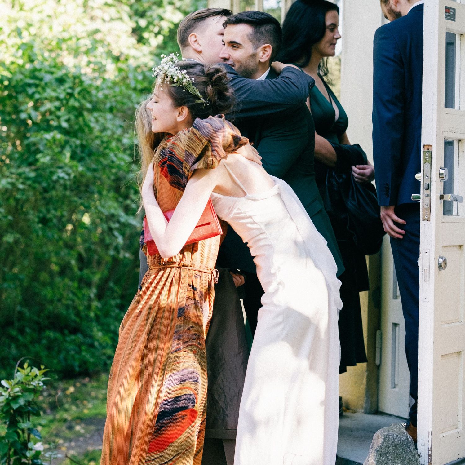 Wedding guests embrace and celebrate outside a building with white doors.