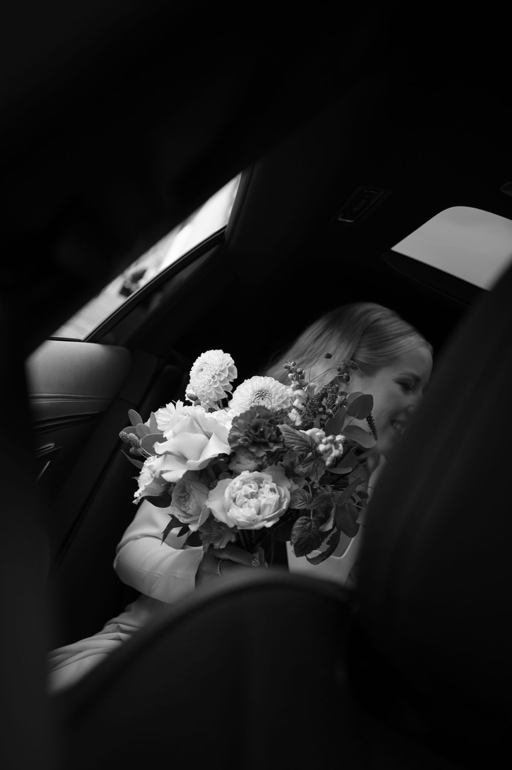 Black and white photo of wedding bouquet resting on car seat.