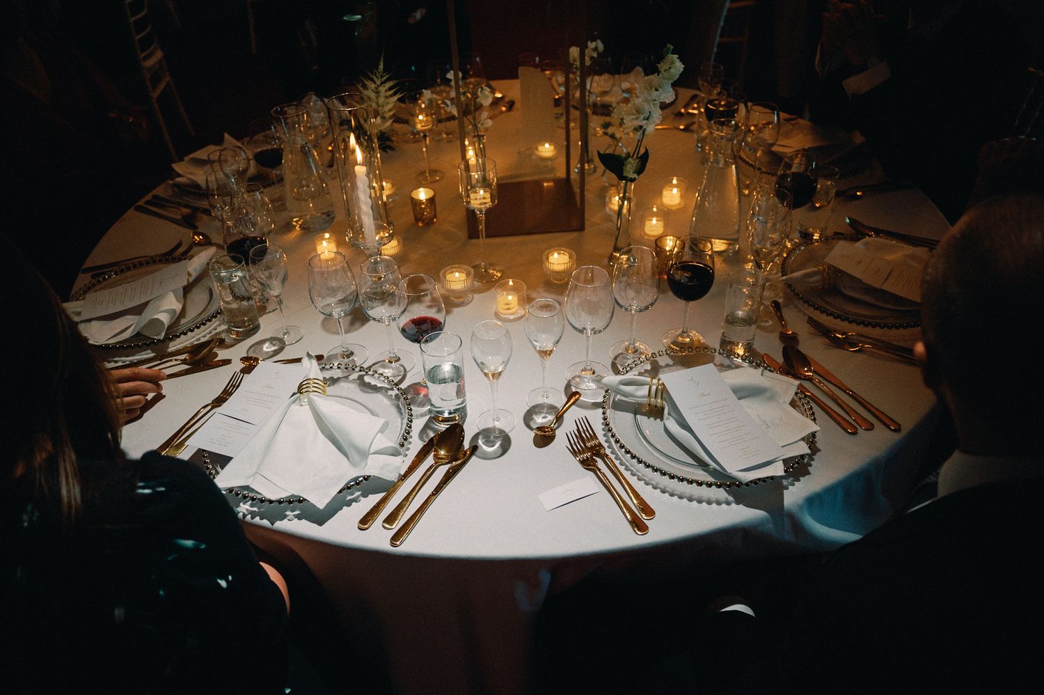 Elegant round dining table set with candles, fine china, and gold cutlery for a formal evening event.