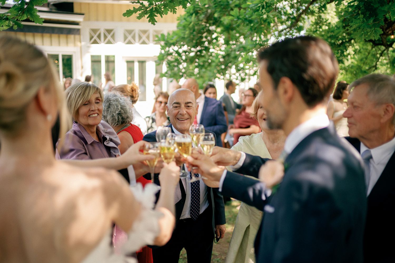 Wedding guests raising champagne glasses in a joyful outdoor toast celebration surrounded by trees.