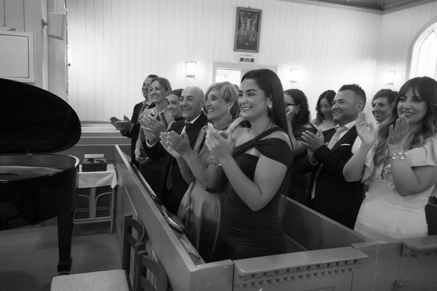 Black and white photo of elegantly dressed guests clapping and smiling at a formal wedding reception indoors.