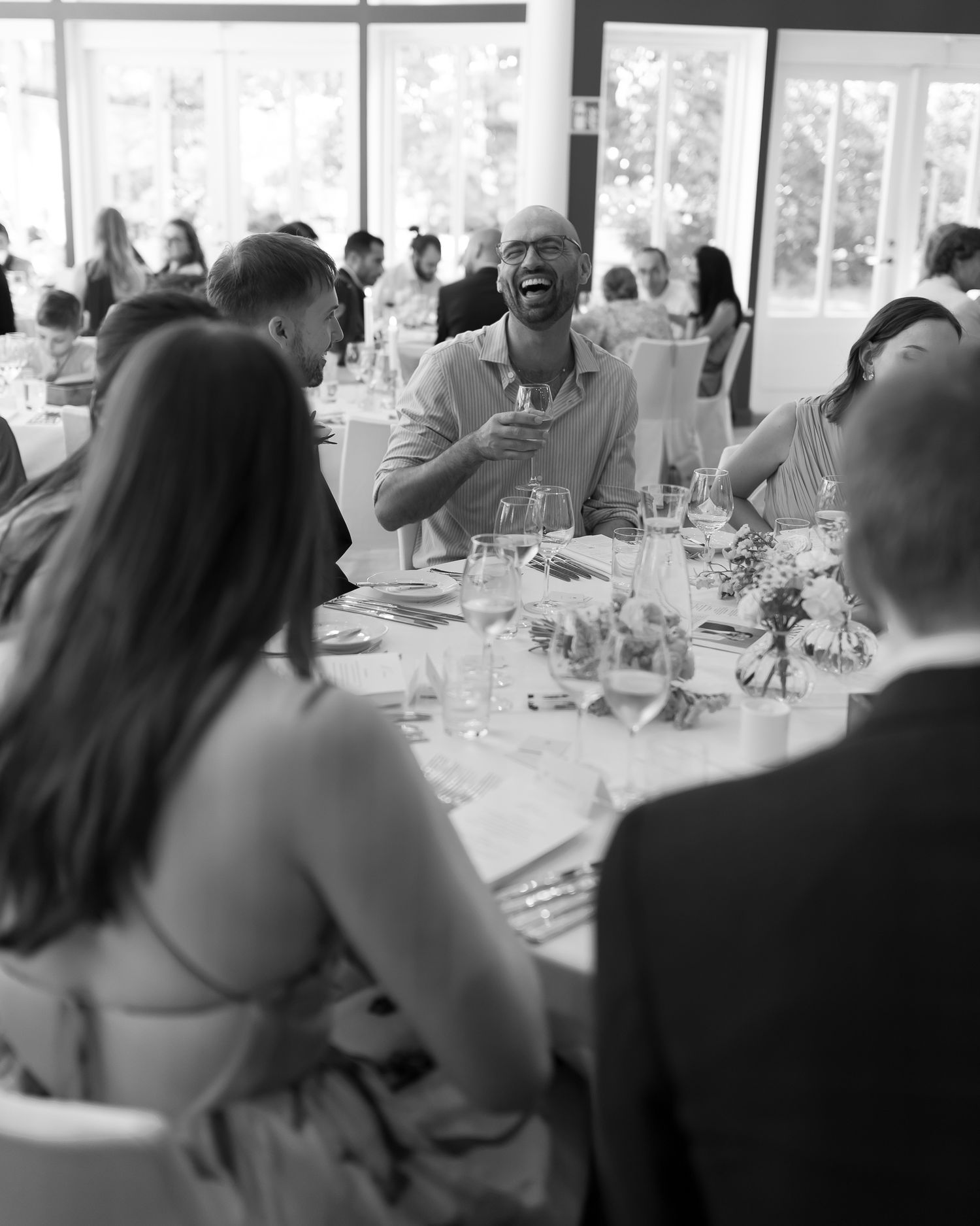 Black and white photo of guests laughing and enjoying drinks at an elegant wedding reception dinner.