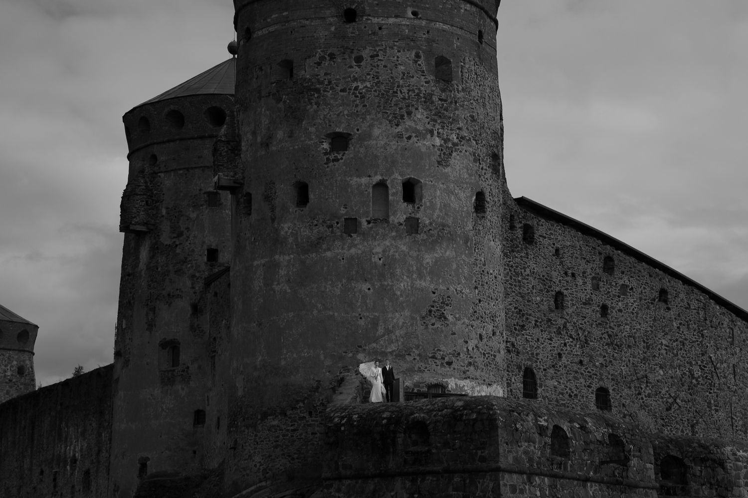 Black and white photo of an ancient stone castle tower with weathered walls and small windows.