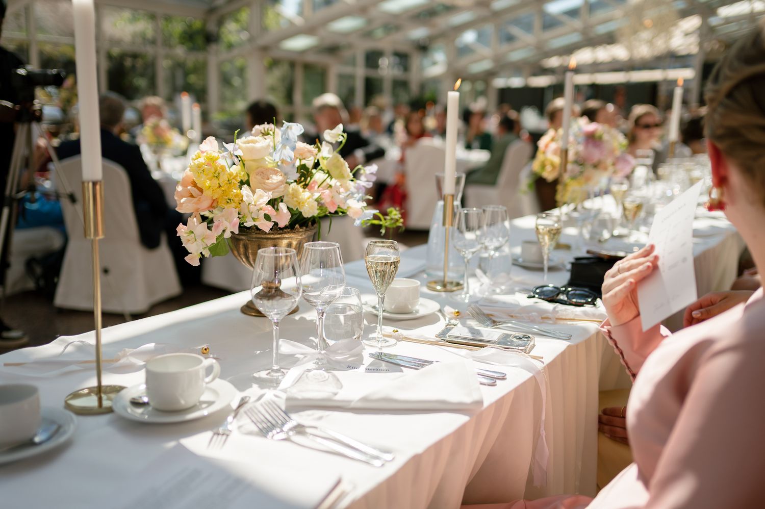 Elegant wedding reception table with white linens, gold candelabras, floral centerpieces, and fine china place settings.