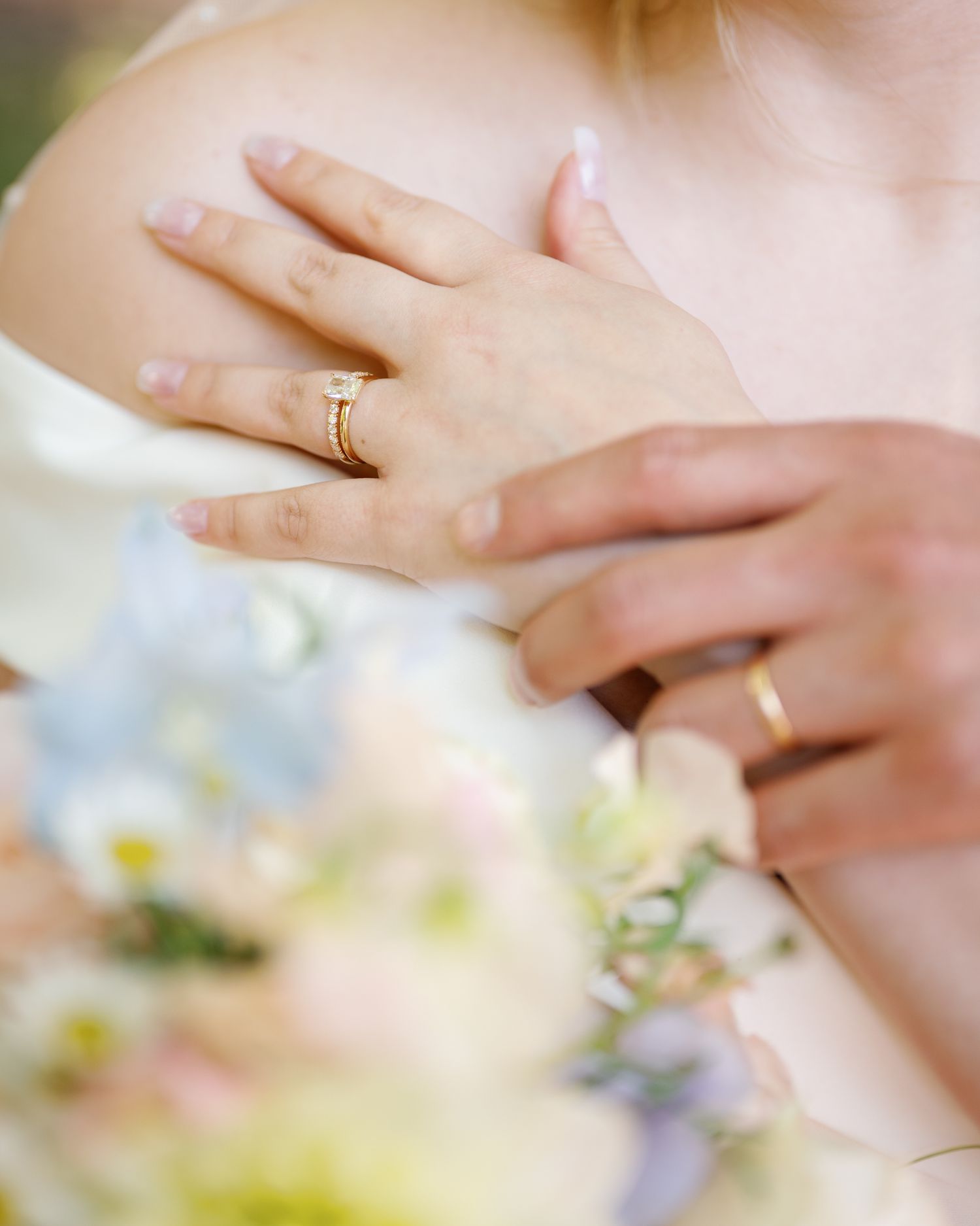Close-up of bride's hands adorned with gold diamond engagement ring and wedding band holding a pastel floral bouquet.