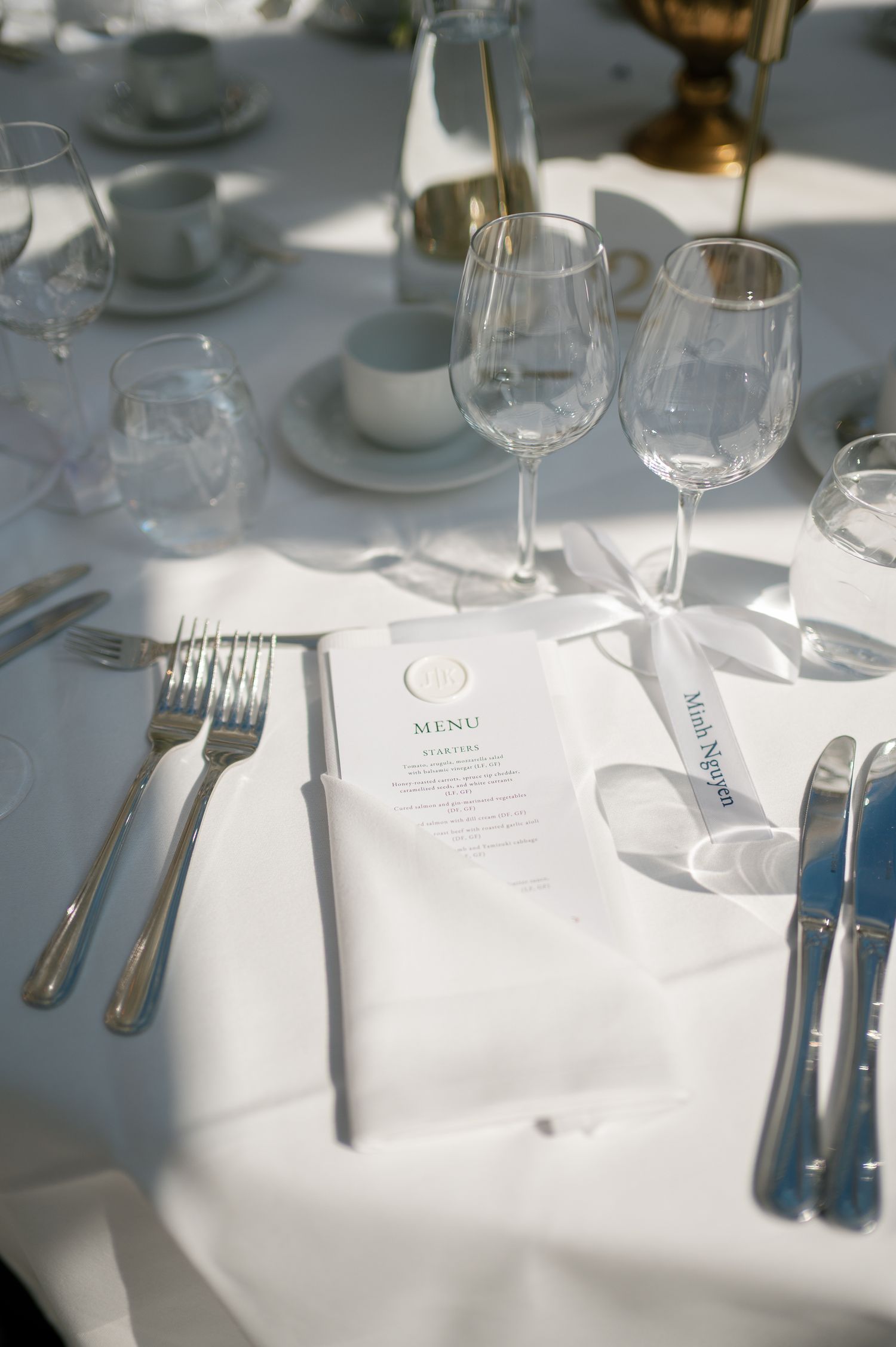 Elegant wedding table setting with white linen, silver cutlery, crystal wine glasses, and a formal menu card.