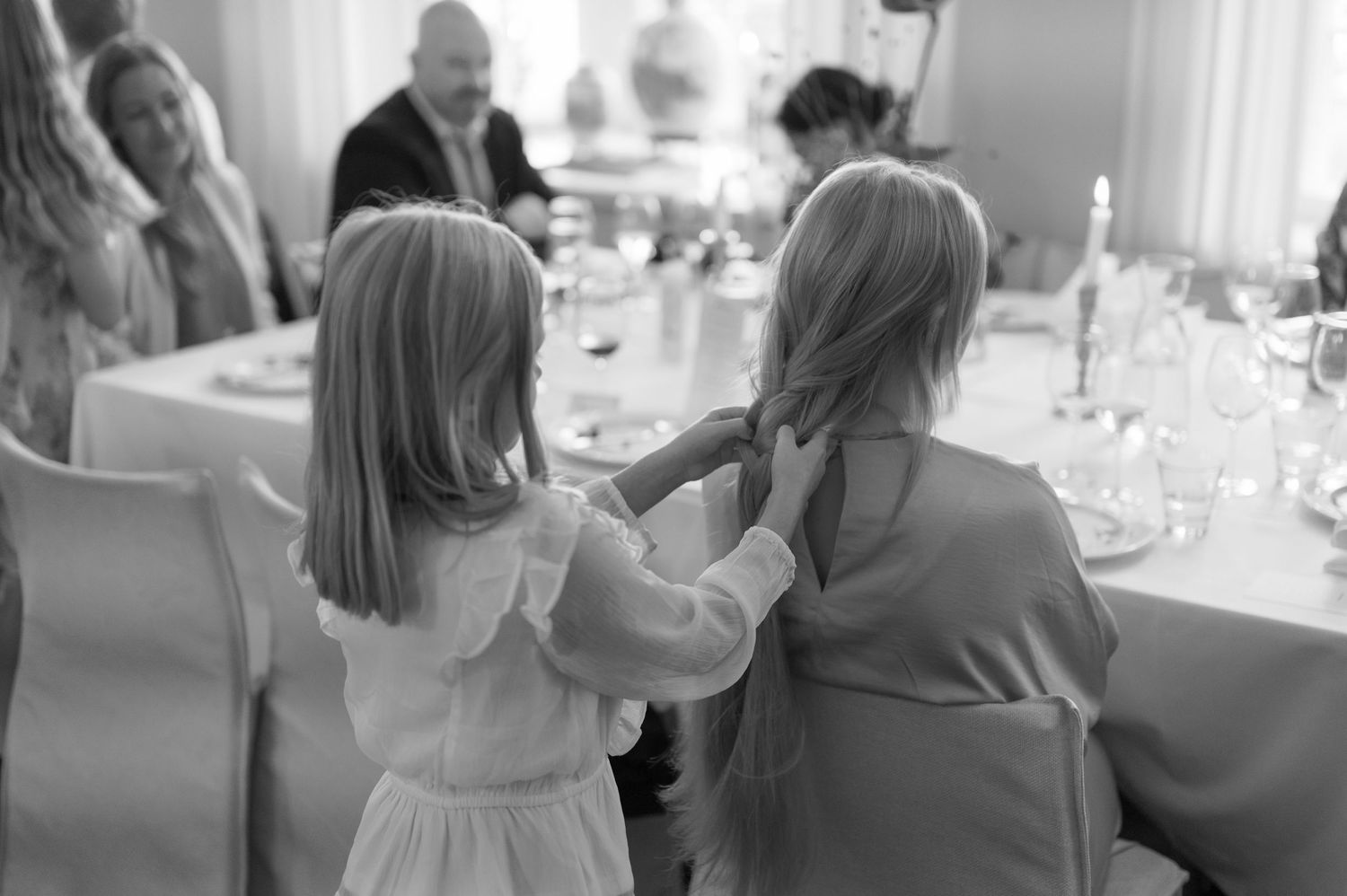 Two young children in formal attire sit at an elegant dinner table with white linens and place settings.