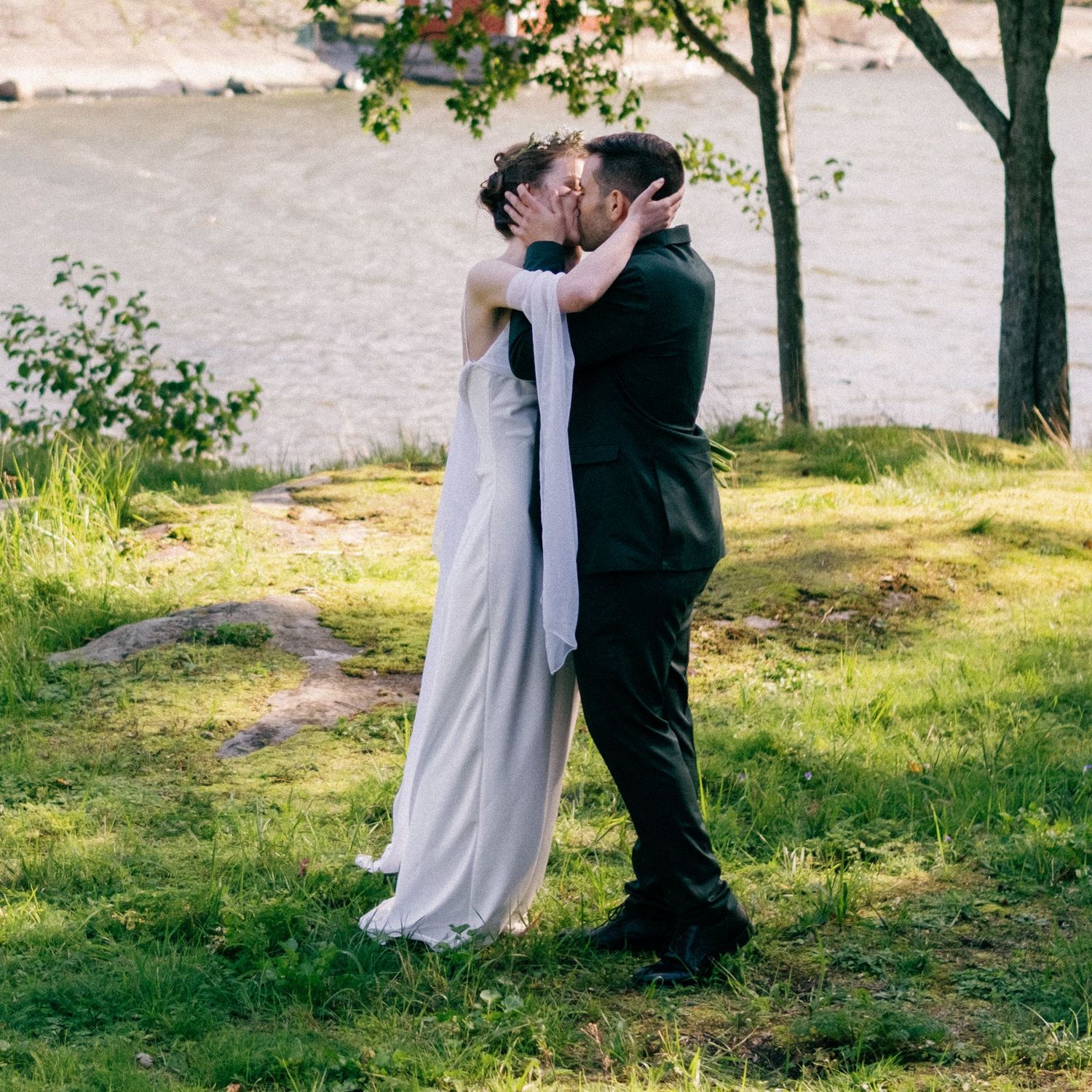A romantic wedding moment captured as couple embraces on a sunny spring day by the water.