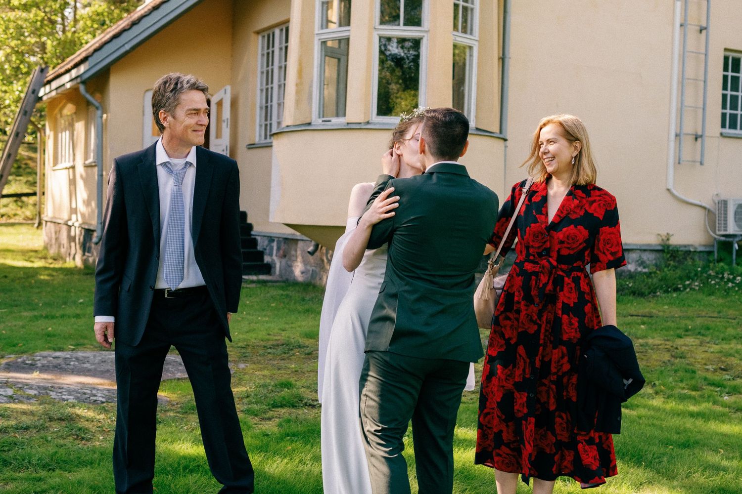 Wedding guests gathered outside a yellow house during an outdoor celebration.