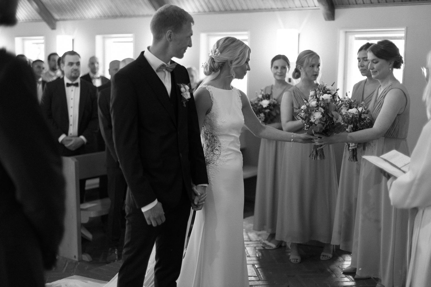 Black and white wedding ceremony photo showing a couple at the altar with attendants.