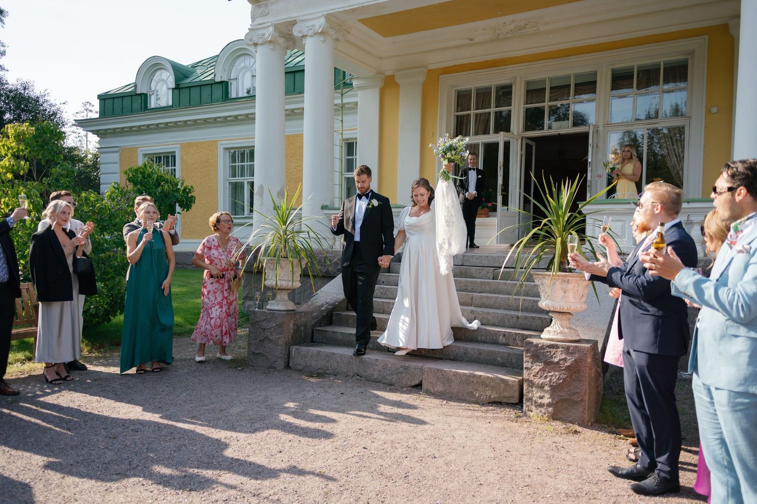 Wedding guests gathering outside yellow mansion during daytime celebration.