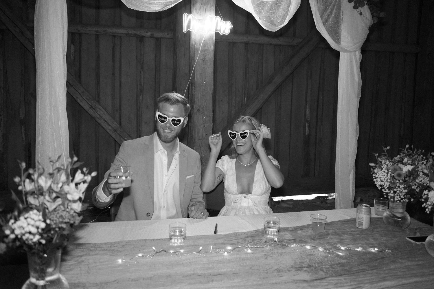 Guests seated at long tables celebrate during an evening barn wedding reception.